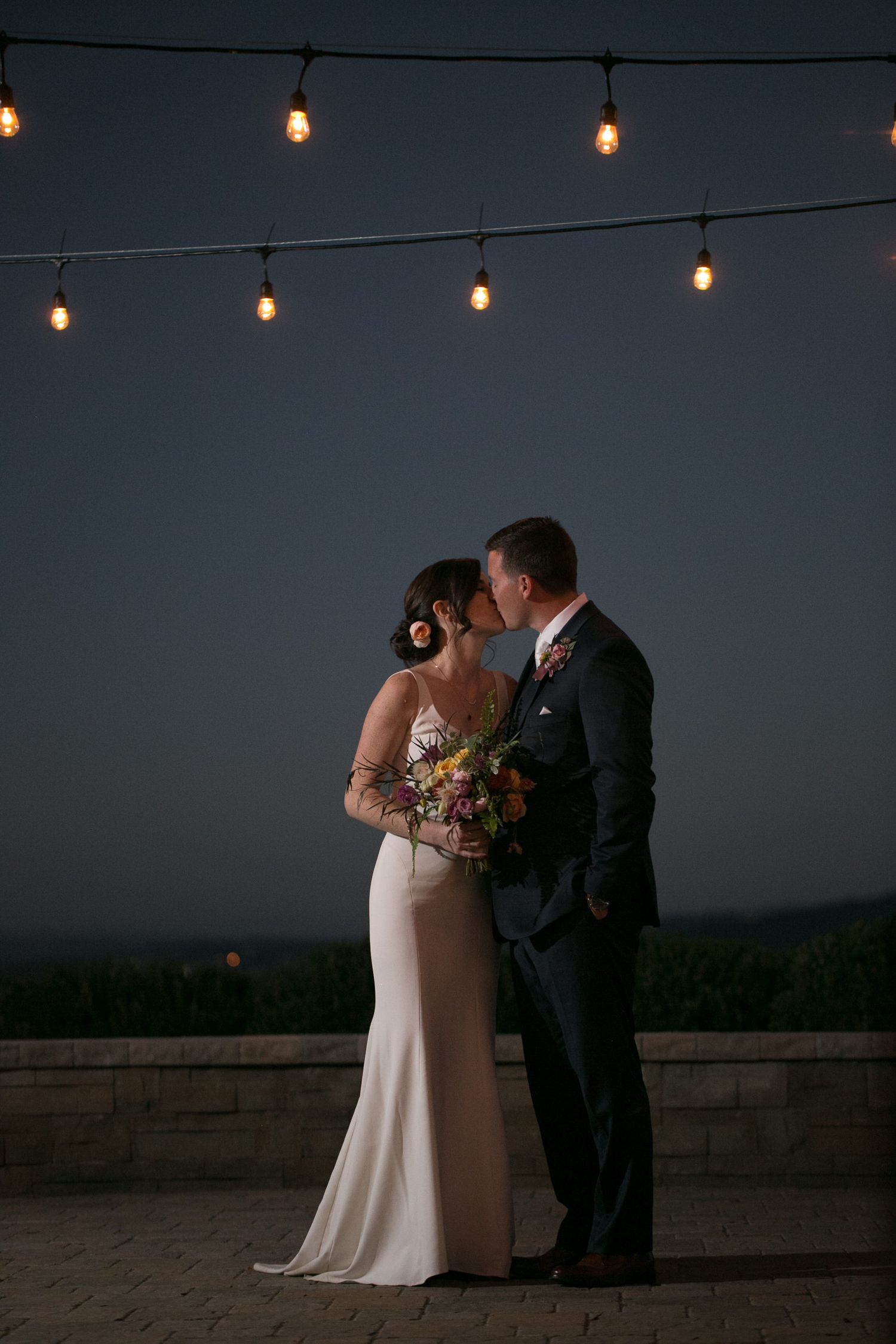 A romantic evening moment under string lights at an outdoor wedding venue.
