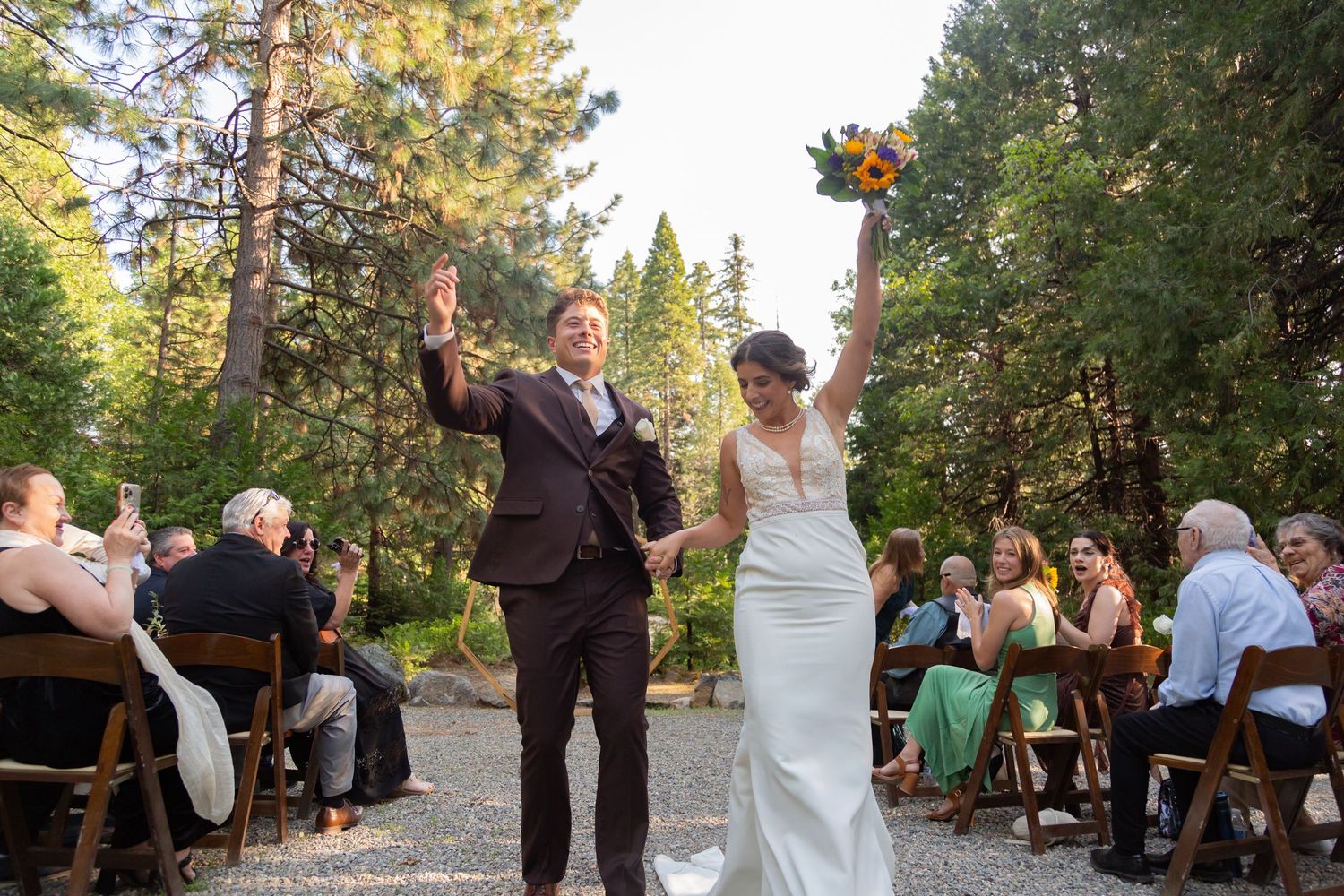 Wedding party celebrates together in a sunlit forest setting on a beautiful summer day.
