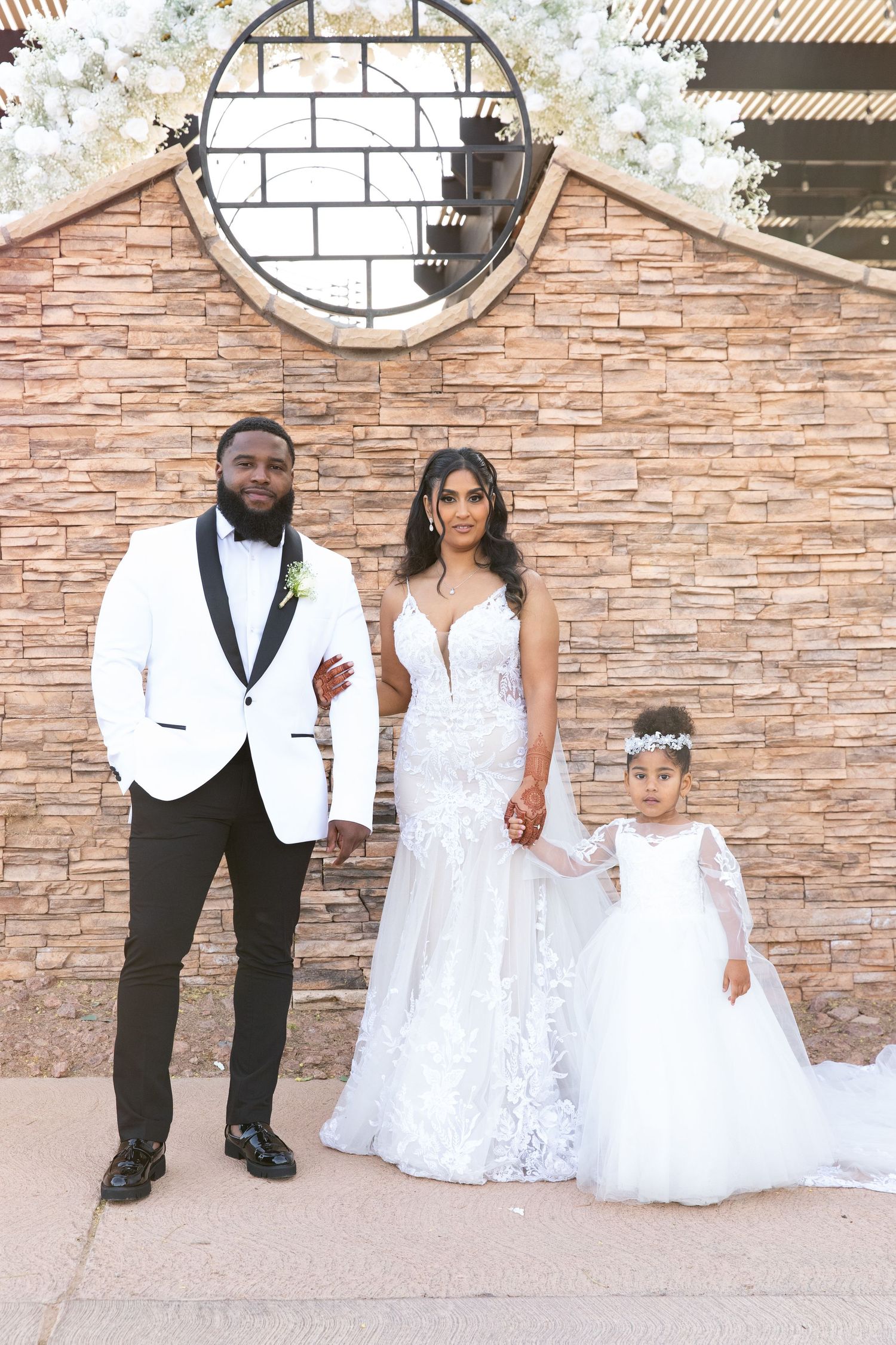 Elegant wedding portrait in front of a stone wall with circular architectural detail.
