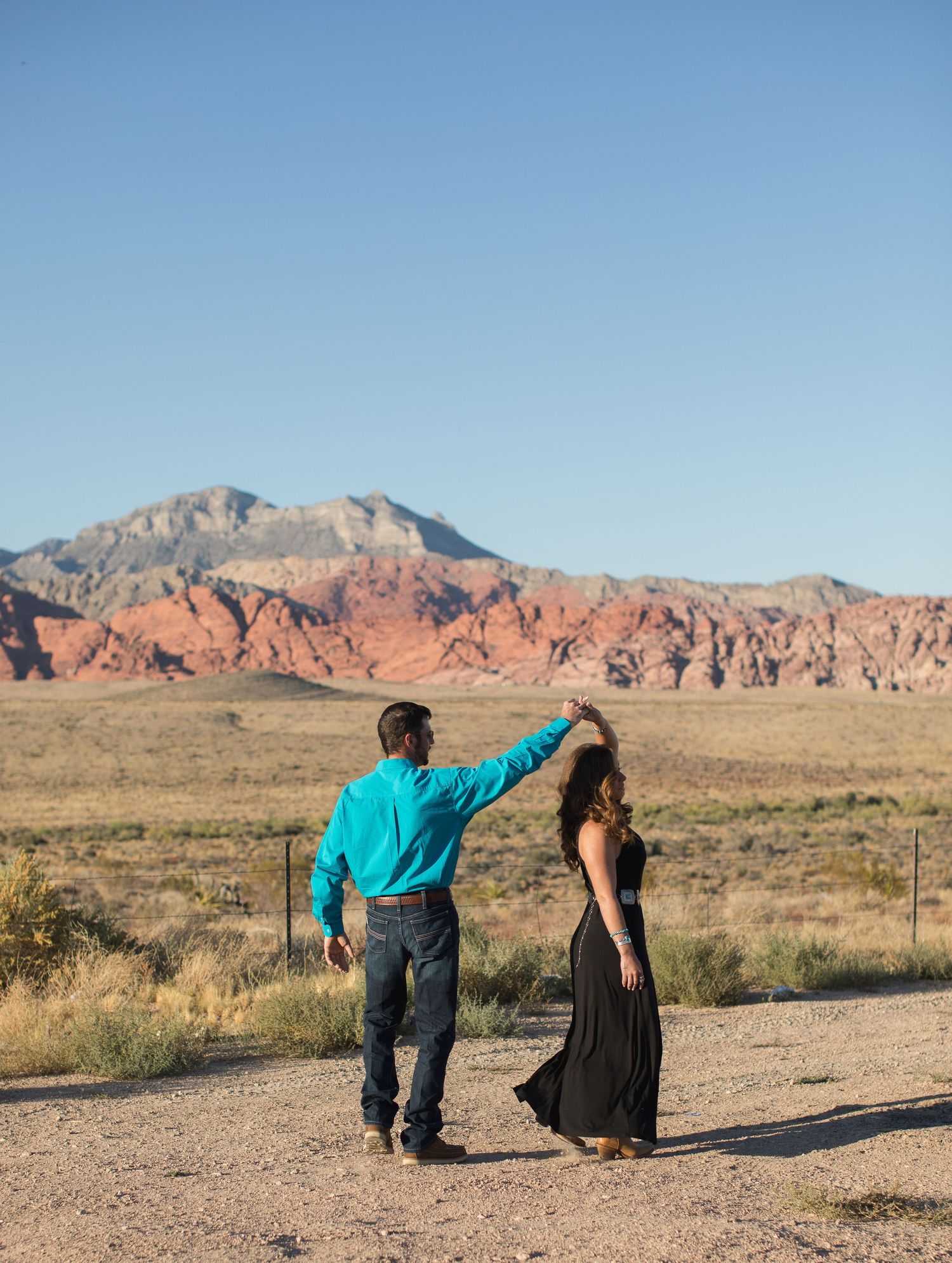 Couple posing dramatically against desert landscape with red rock formations in background.
