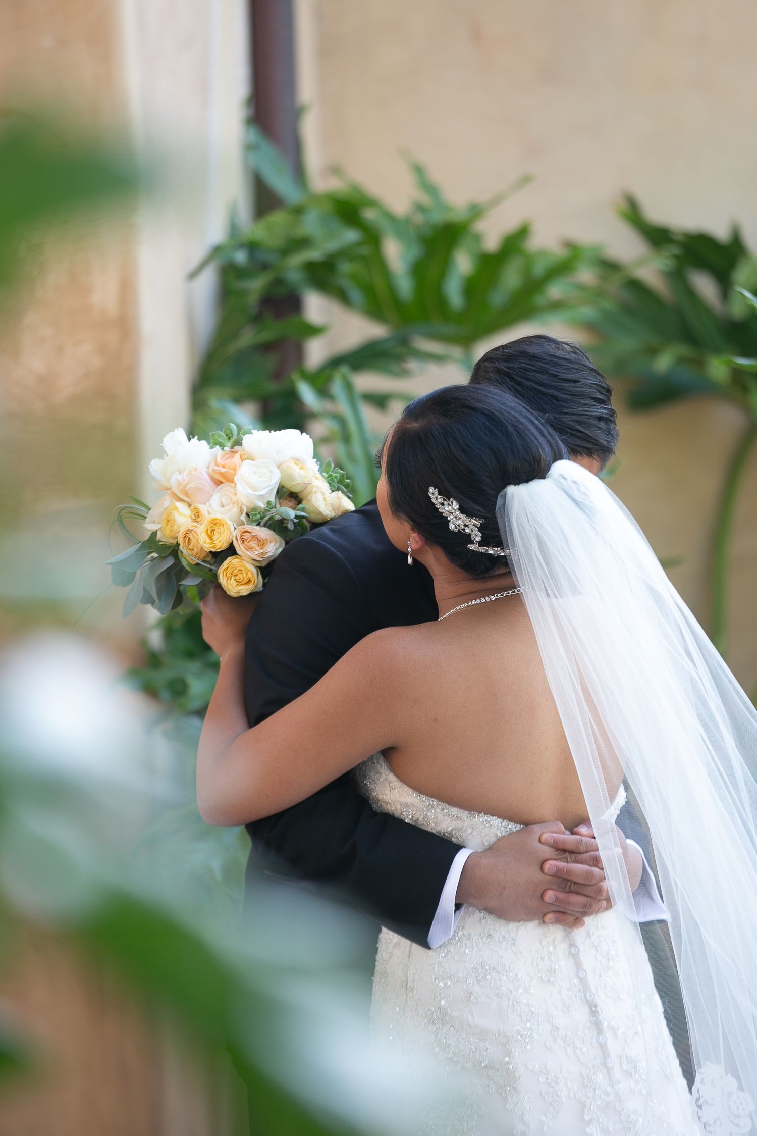 A tender embrace between newlyweds with a peach and white bouquet.
