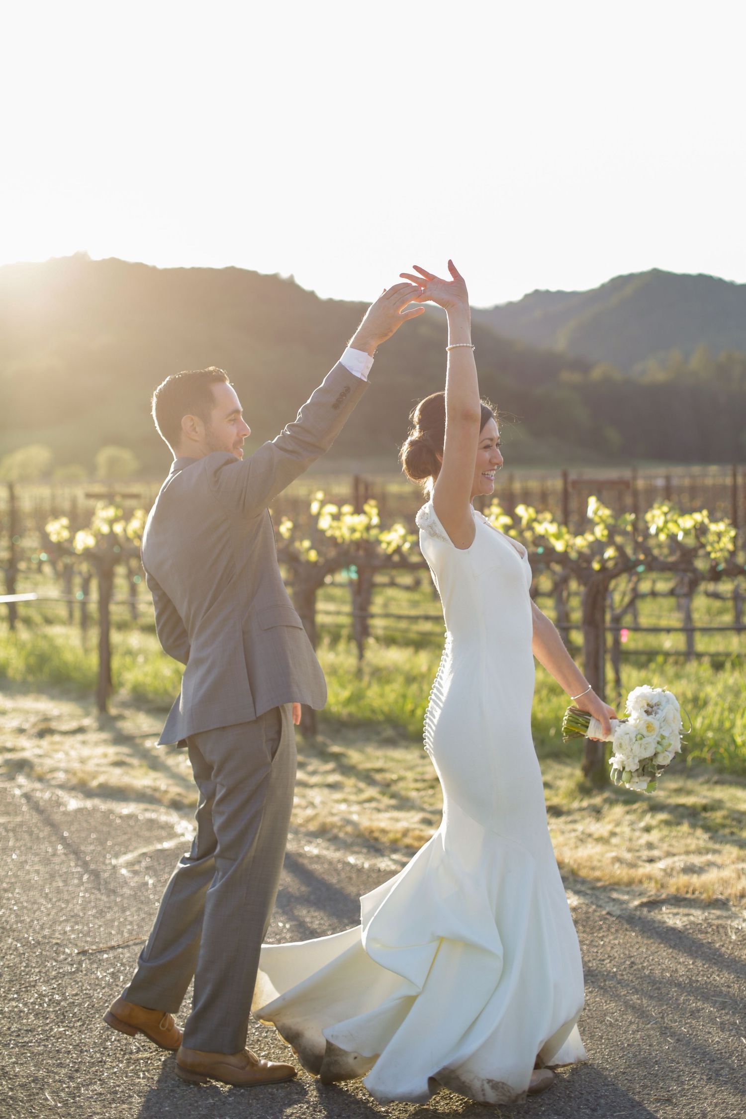 A couple dances in a vineyard at sunset, with the bride's dress flowing elegantly.