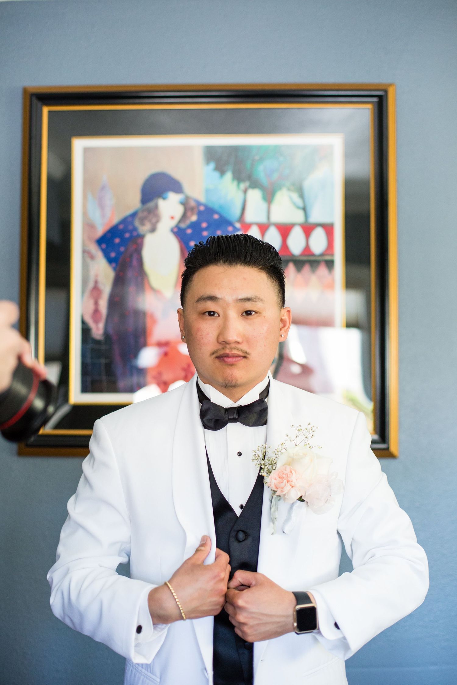A groom in a crisp white tuxedo jacket and bow tie poses for a formal portrait.