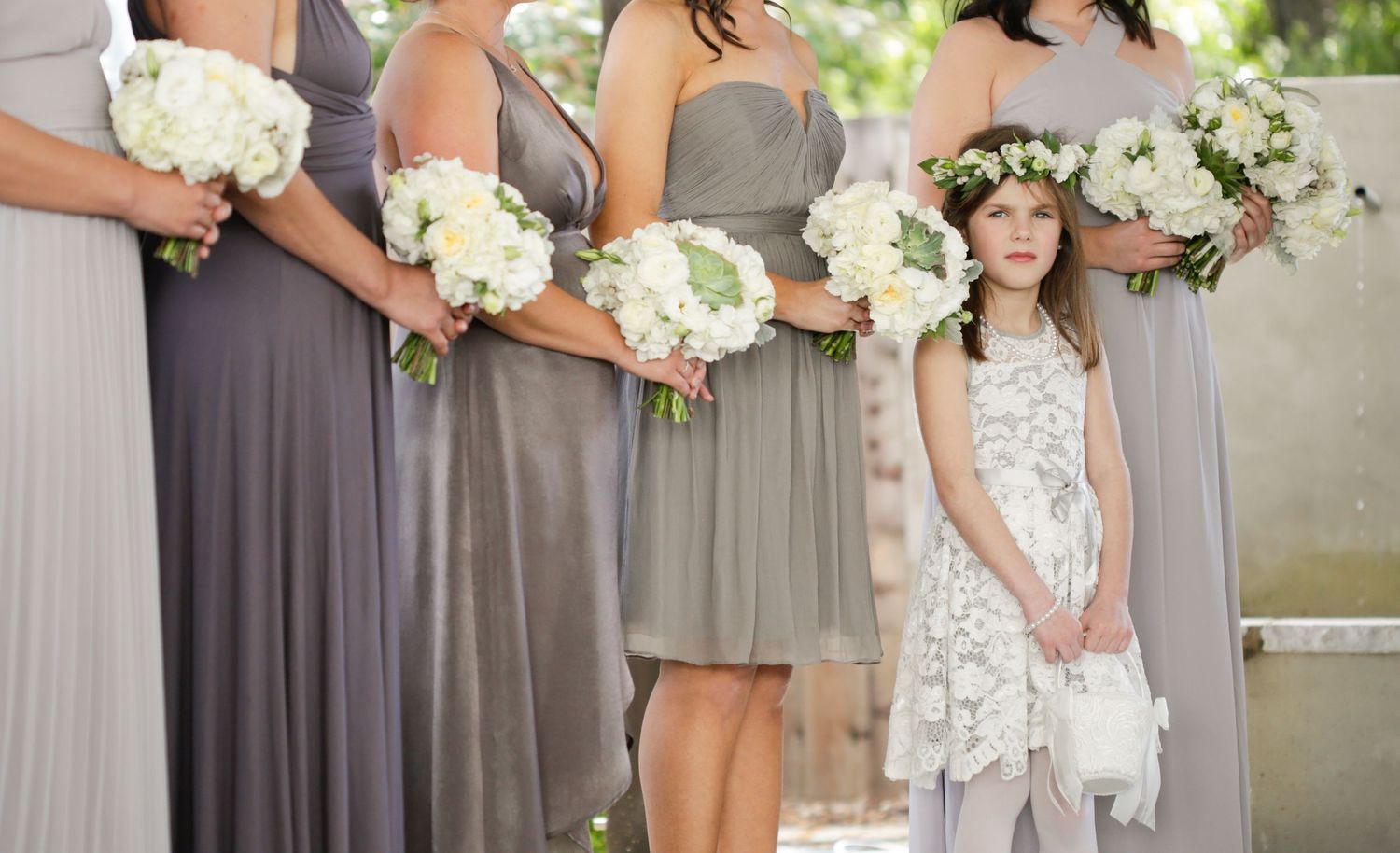 Wedding party members in coordinated gray dresses hold white floral bouquets.