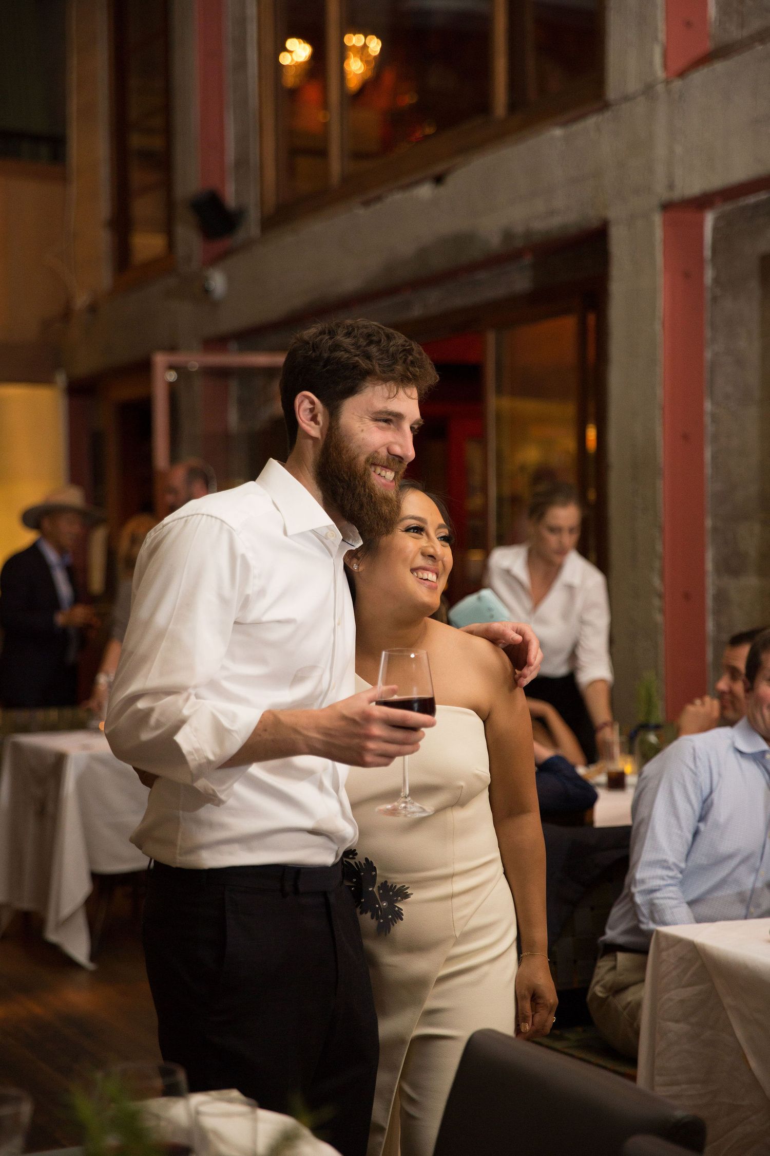 A couple shares a joyful moment during their wedding reception, dressed in elegant white attire.