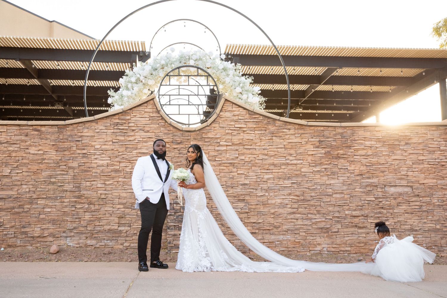 Bride and groom pose under an elegant stone archway at sunset.