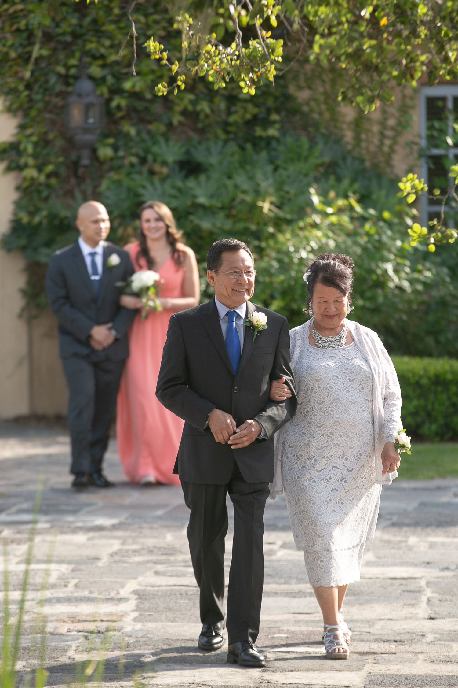 Wedding party members walking down a garden path in formal attire.