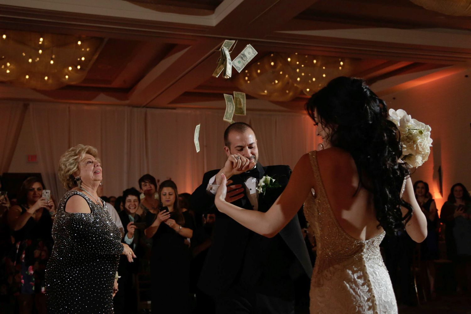 Wedding party celebrating on the dance floor with ambient lighting and string lights in the background.