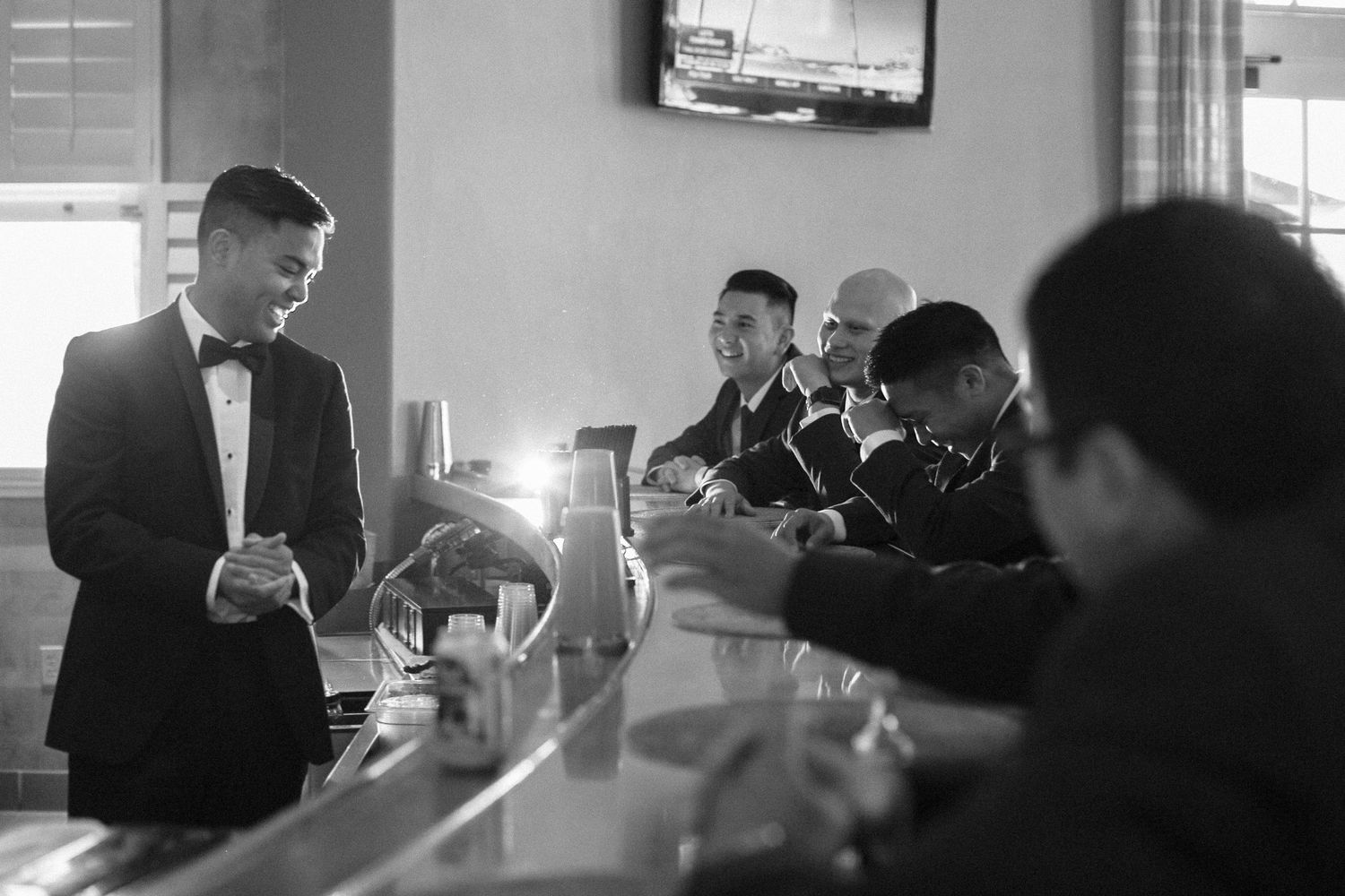 A black and white photo of guests mingling at a bar in formal attire.