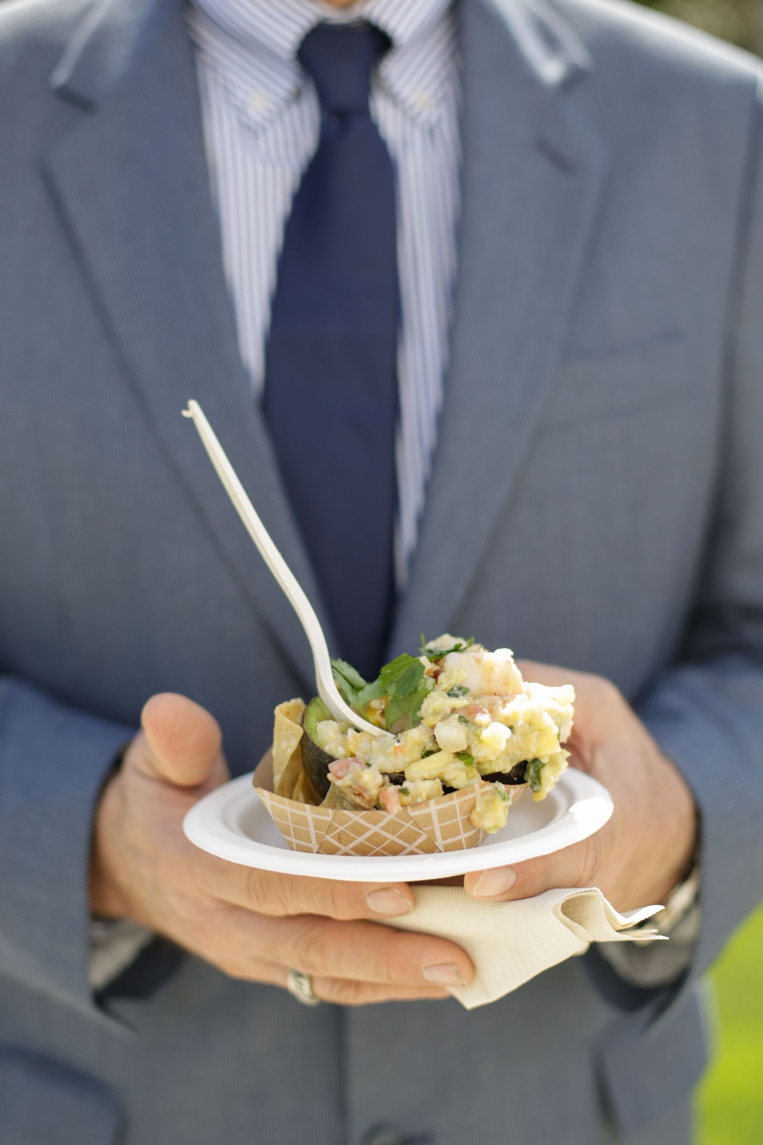 Close-up of wedding guest in gray suit holding a plate of appetizers.