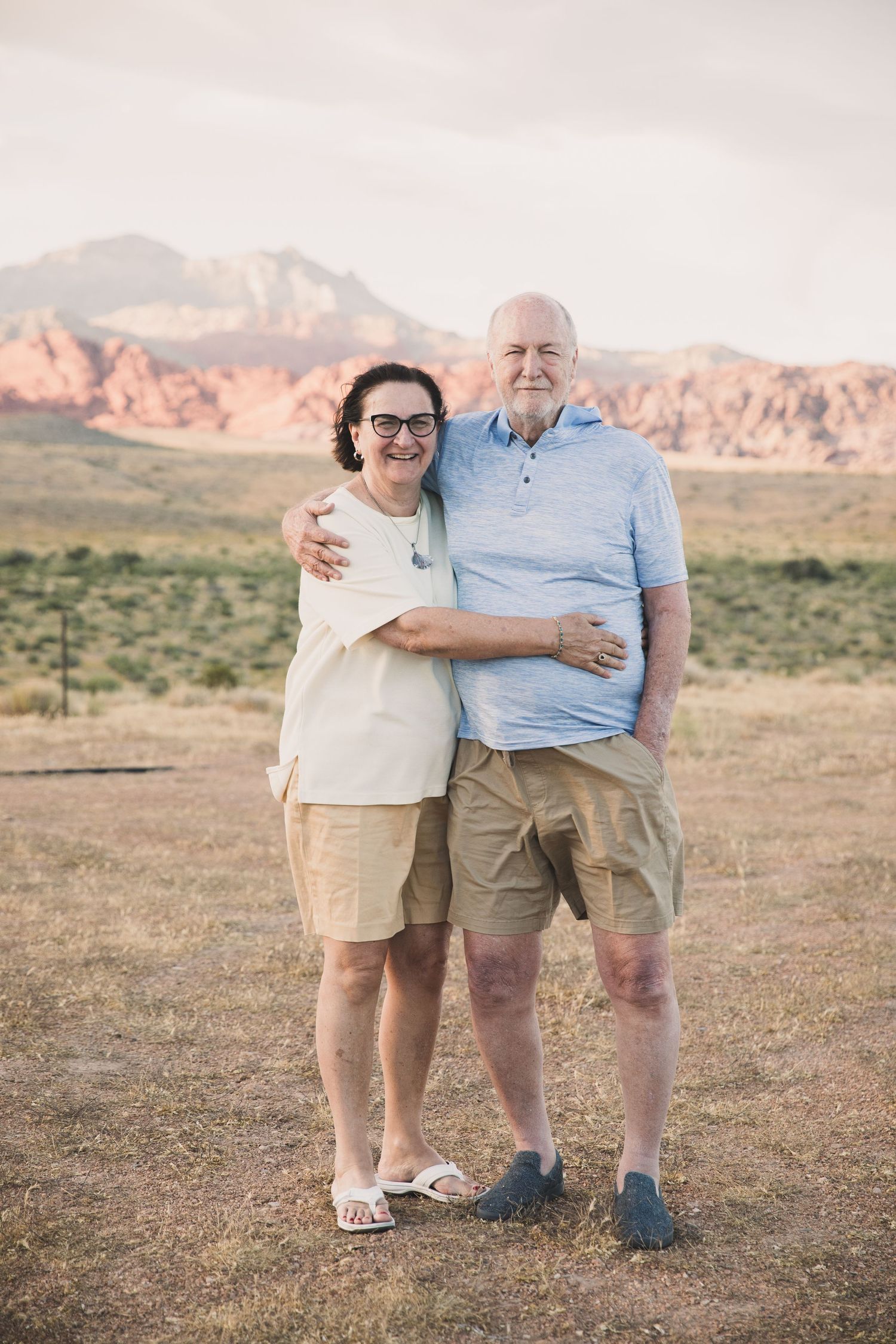 Elderly couple posing together in casual wear against red rock formations in the desert.