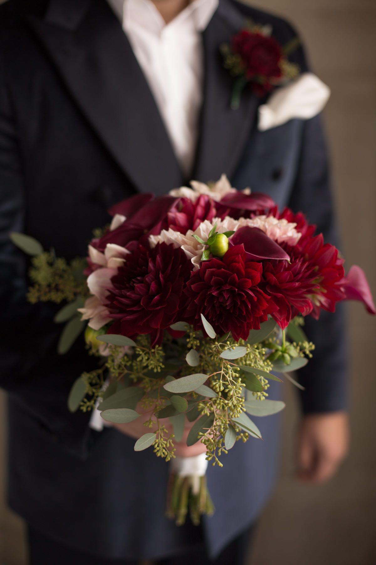 Dramatic burgundy and pink floral arrangement held against a dark navy suit.