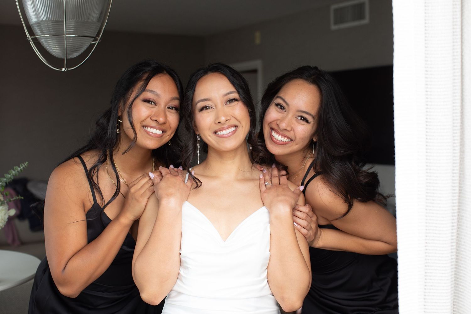 Three women in black dresses and white dress share a moment during a special occasion.