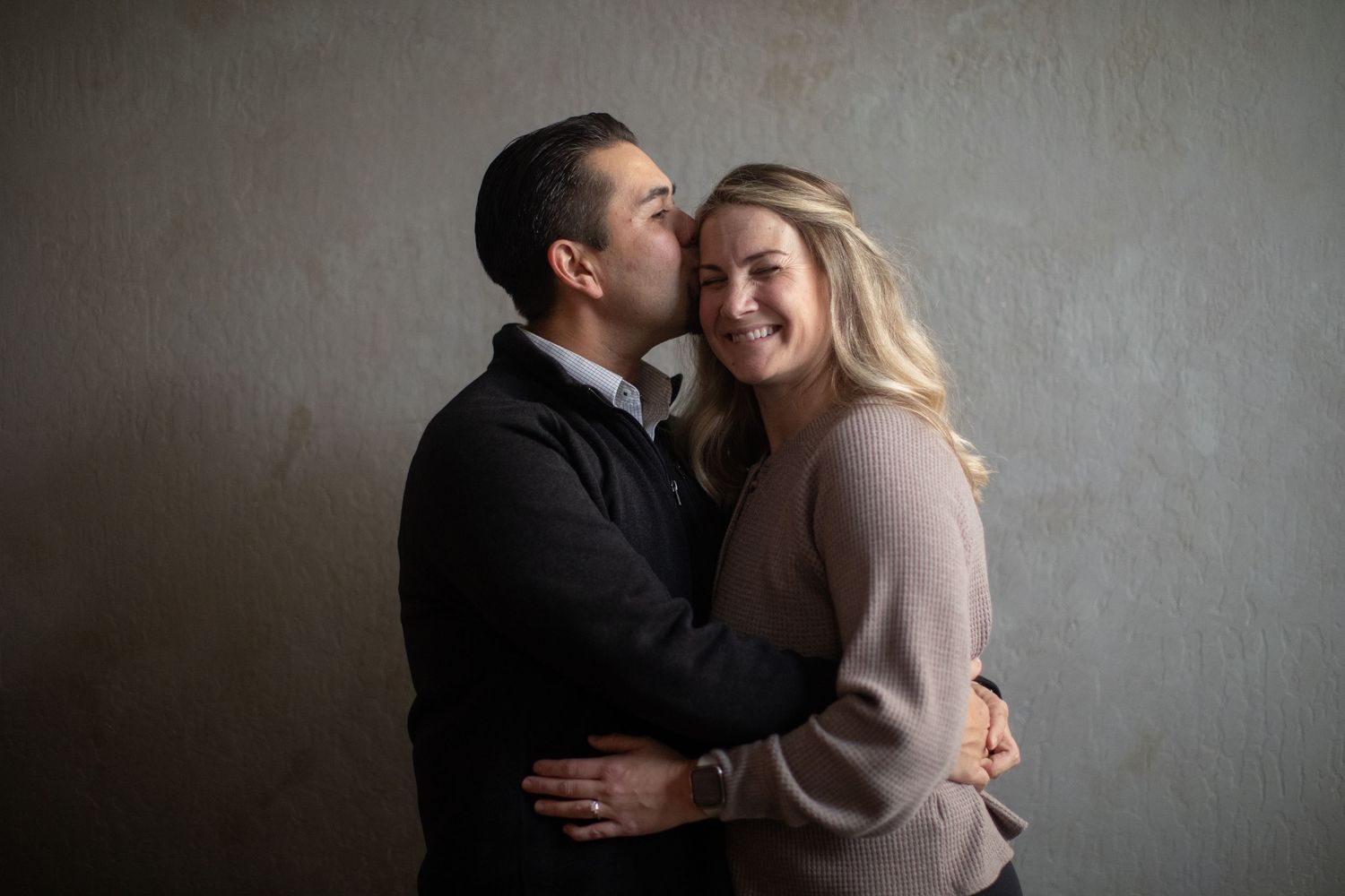 Intimate couple portrait against grey wall in warm sweaters.