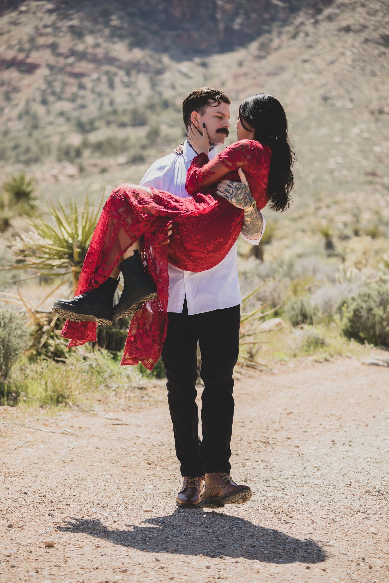 Playful desert photoshoot with partner lifting person in flowing red dress.