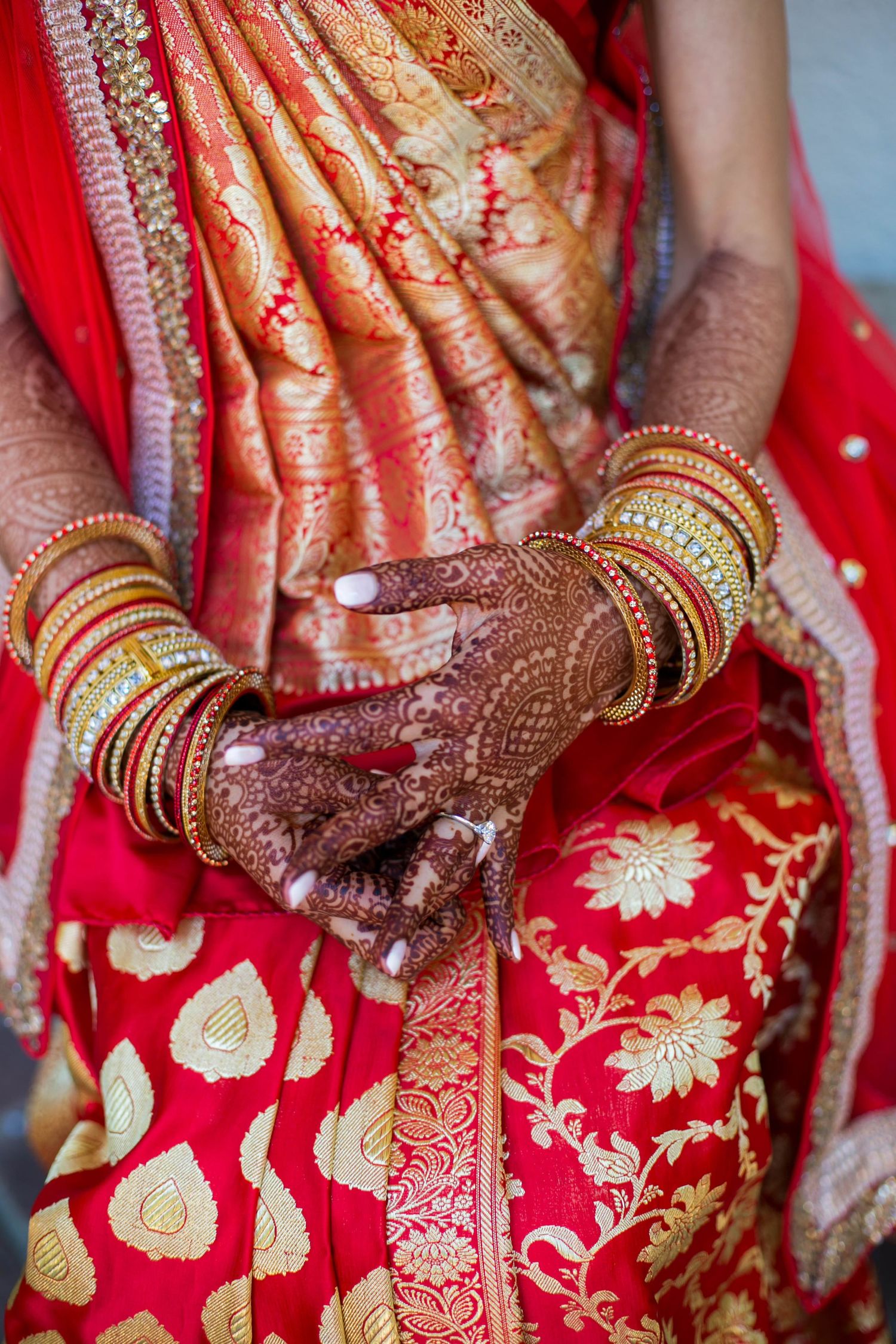 Close-up of intricate henna designs and gold bangles on hands with red and gold sari fabric.