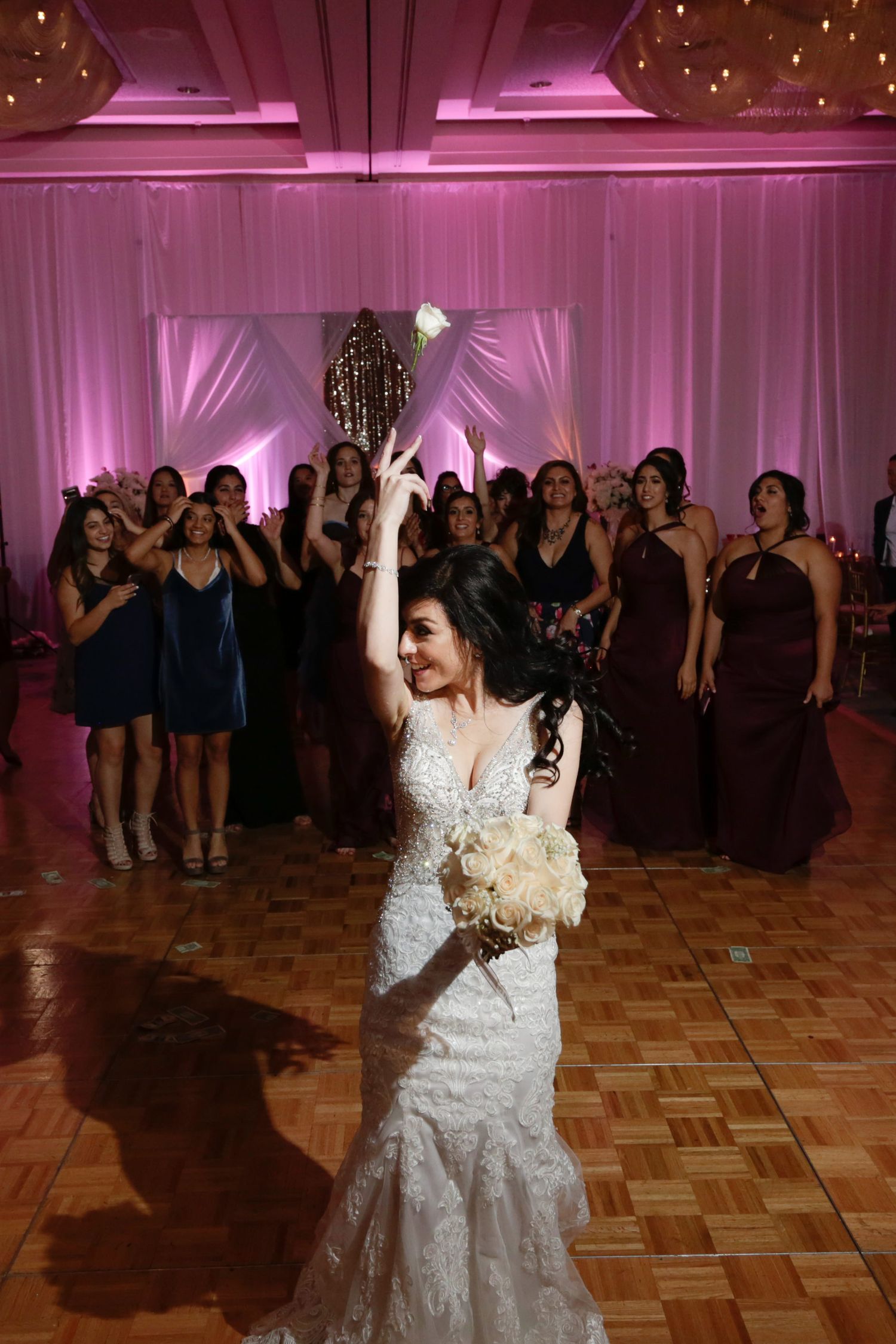 Bride tossing bouquet at wedding reception with pink uplighting and parquet dance floor.