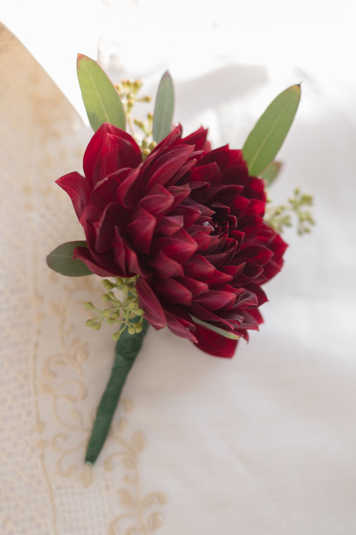 Single deep red dahlia boutonniere with green leaves wrapped in floral tape.