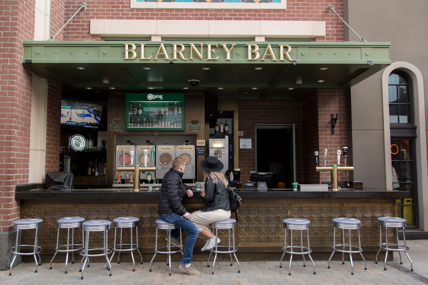A brick facade with a Blarney Bar storefront featuring retro-style bar stools along an outdoor counter.