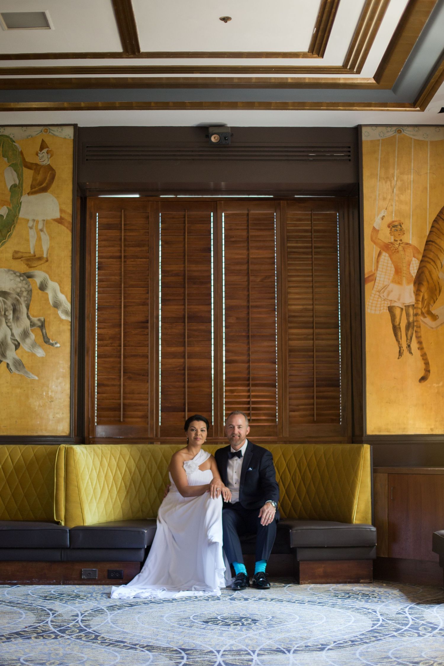 A wedding couple seated on yellow bench with decorative Asian-inspired wall murals.