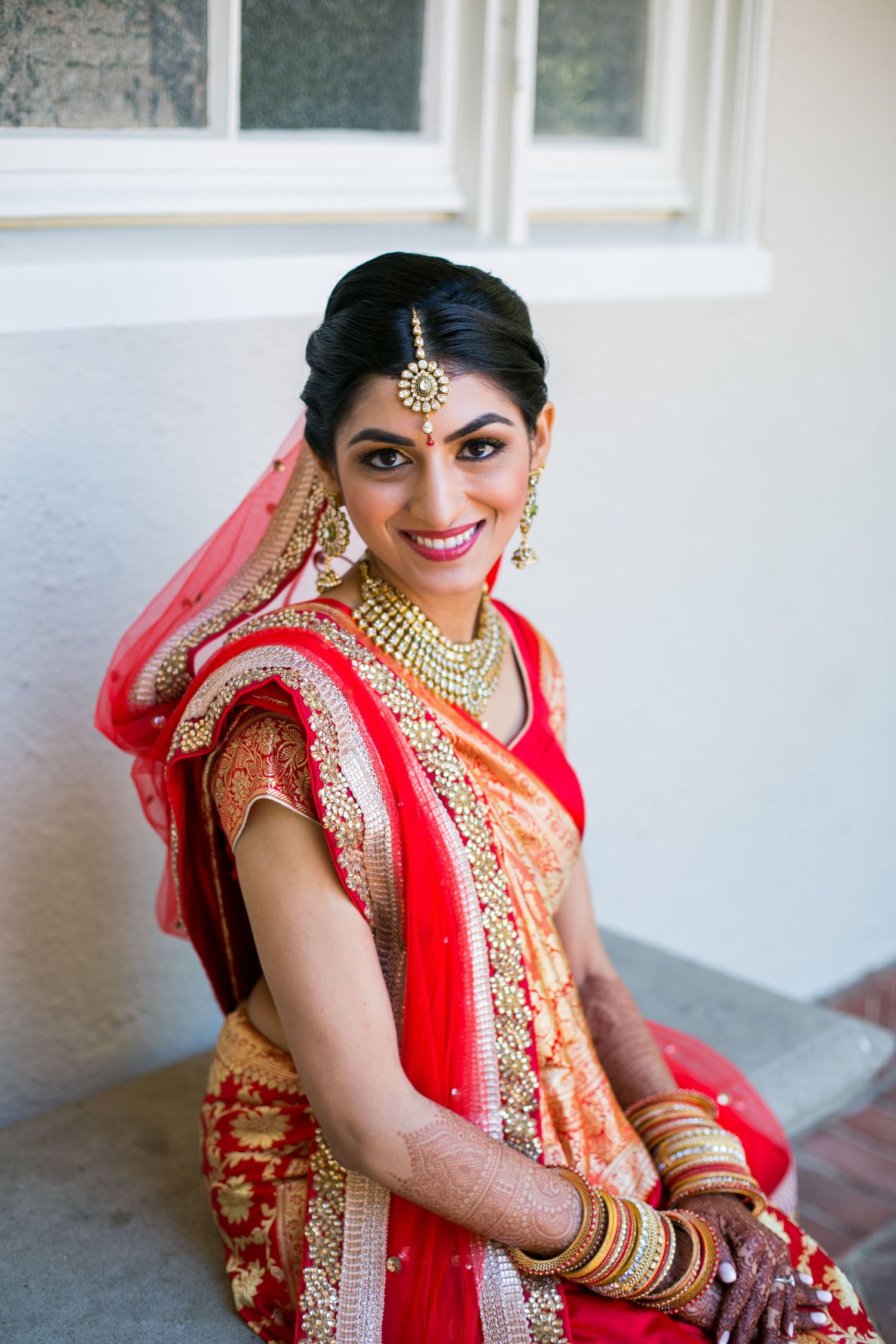Traditional Indian bride in red and gold sari with elaborate jewelry and accessories.
