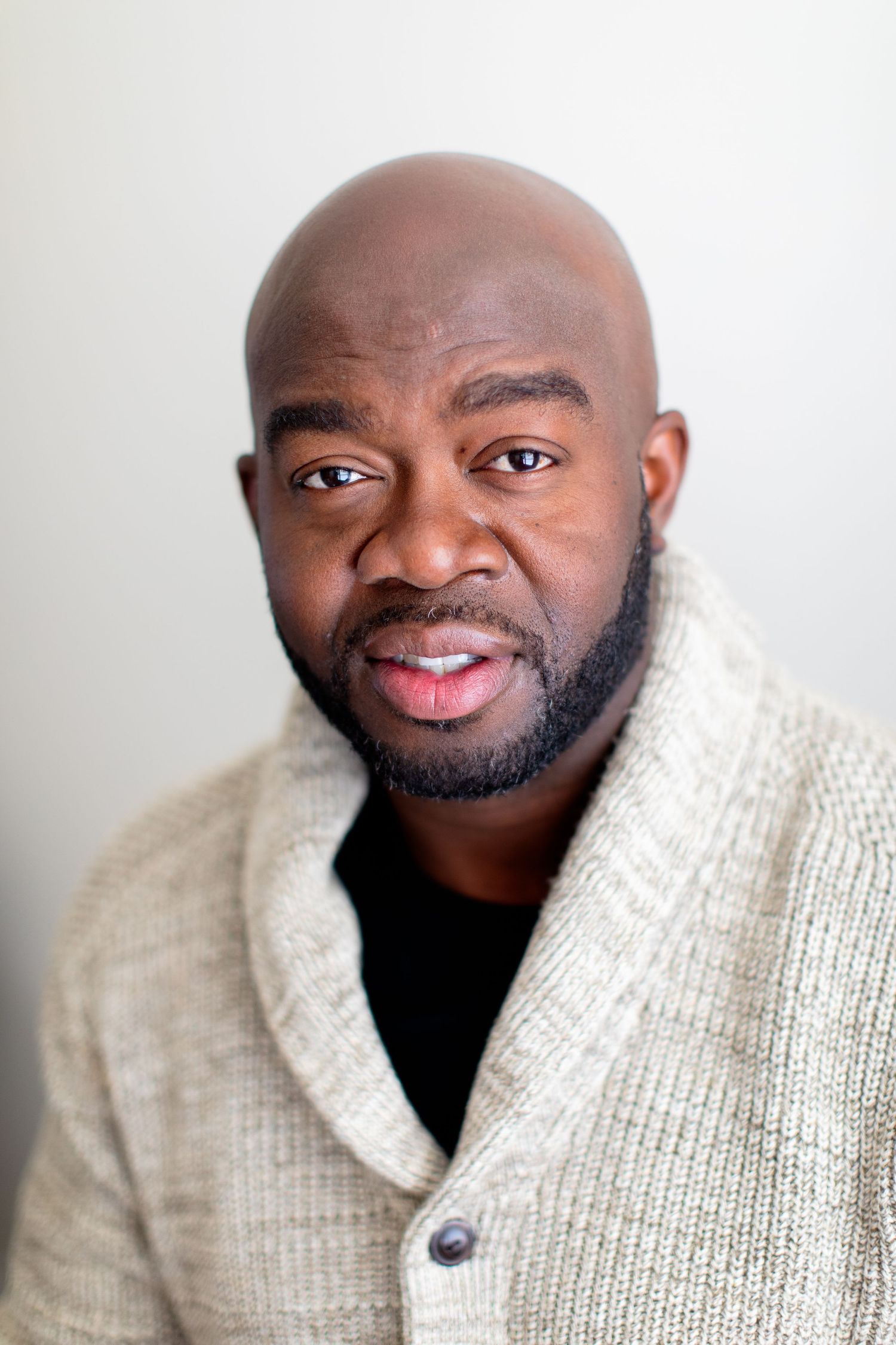 Portrait of person wearing cream cardigan sweater against light background.