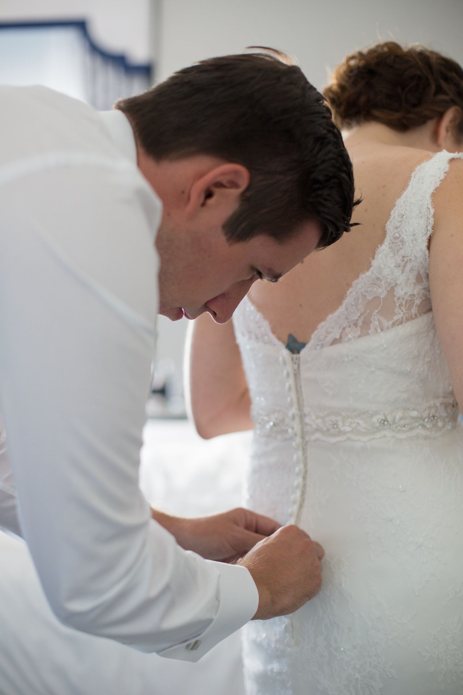 A person in white adjusts the lace details of a wedding dress.