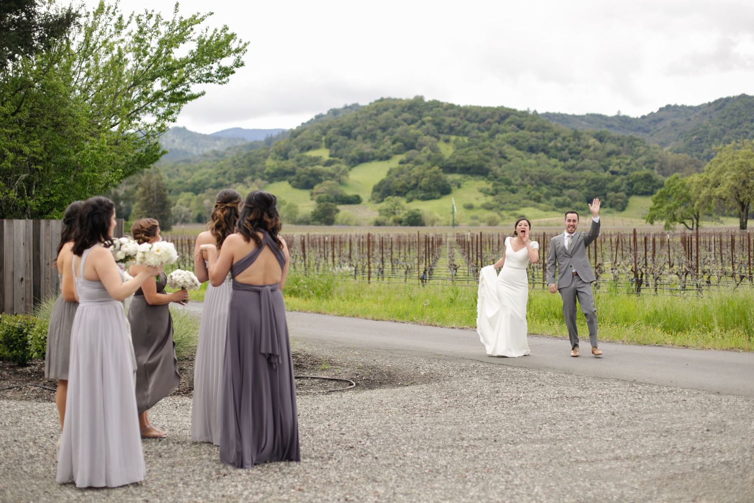 Wedding party members walking along a gravel path with mountains and greenery in the background.