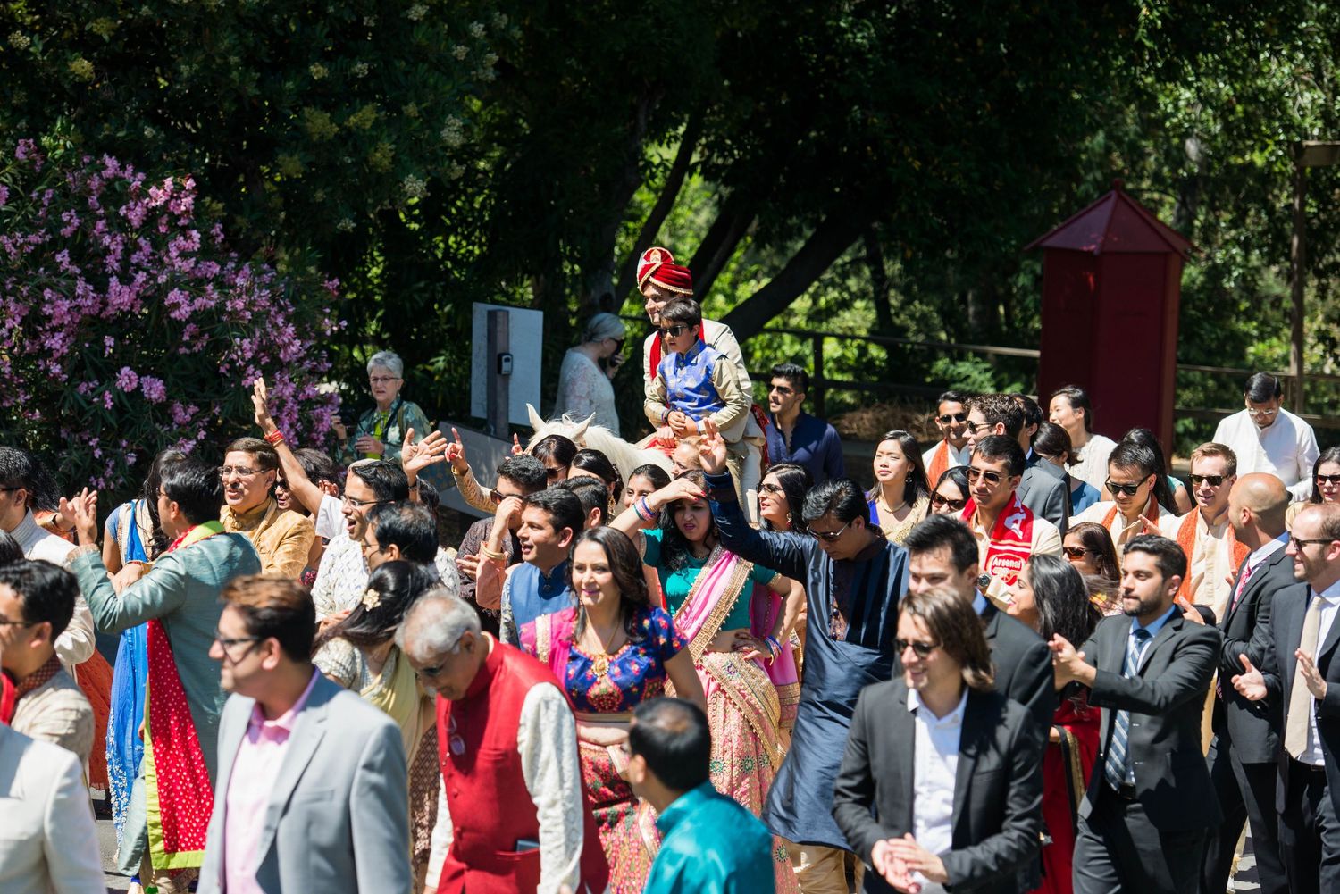 Large outdoor wedding gathering with guests in colorful attire watching a ceremony.