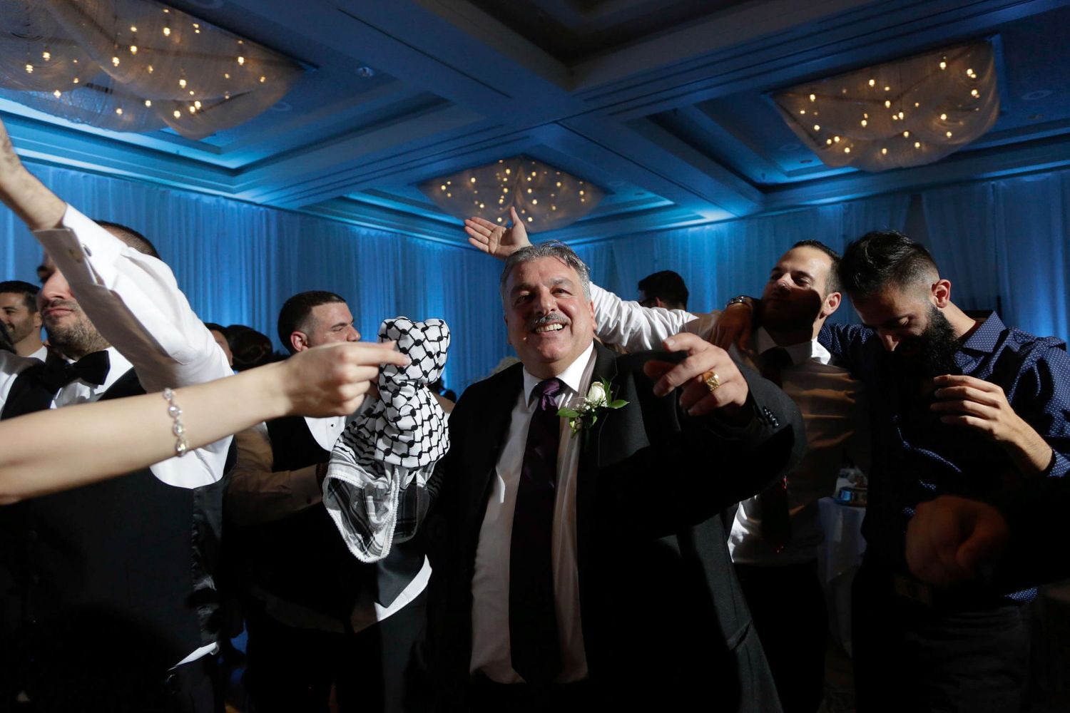 Energetic wedding reception dance party with guests celebrating under blue lighting.