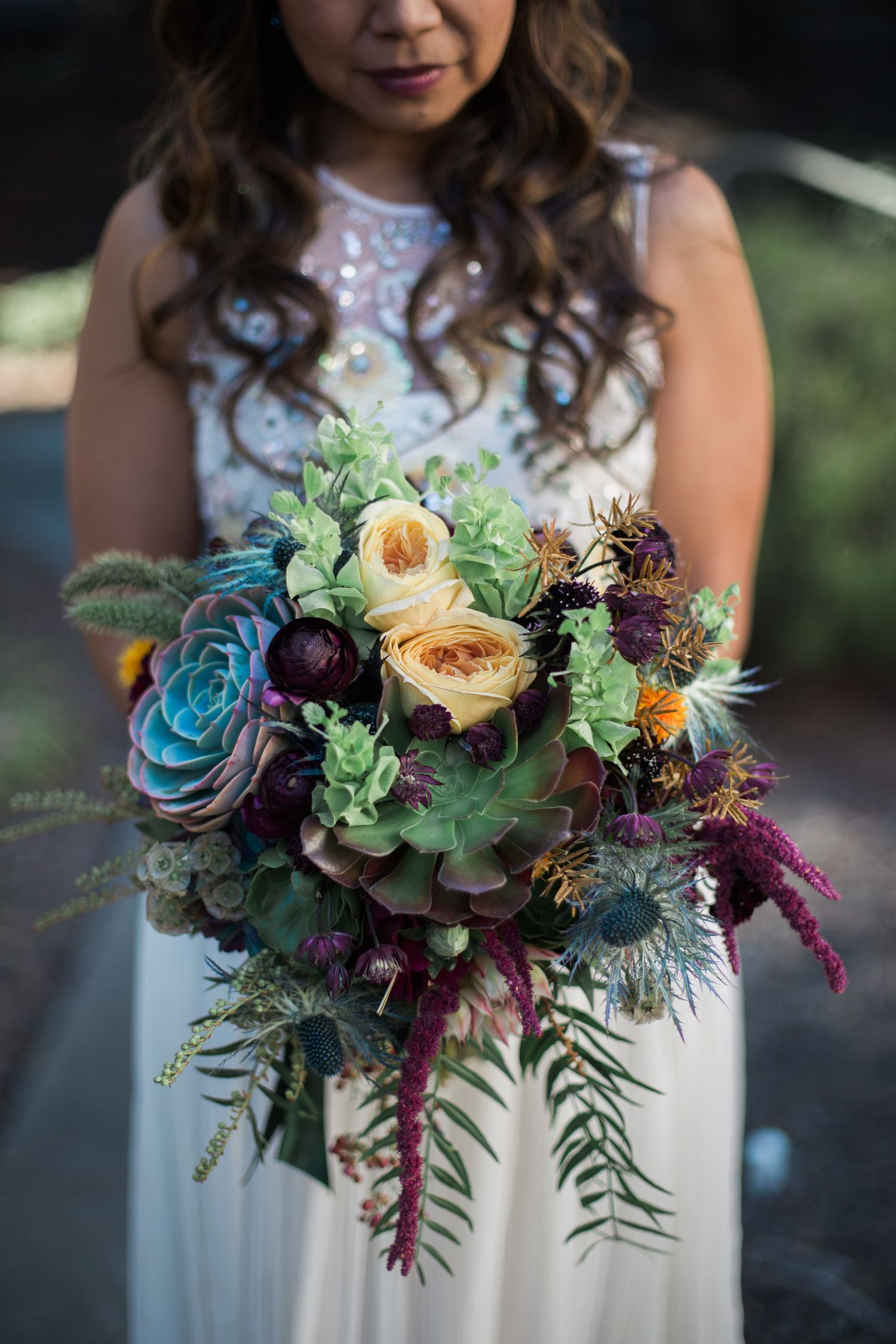 Colorful bridal bouquet with succulents, roses, and deep burgundy flowers.