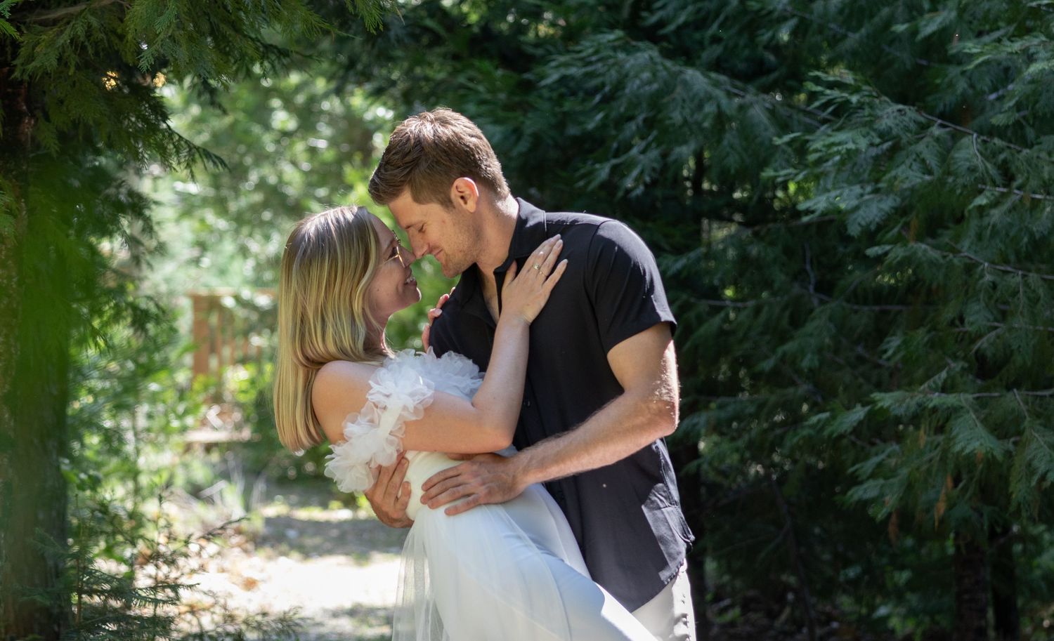 A romantic outdoor portrait of a couple embracing among green trees and foliage.
