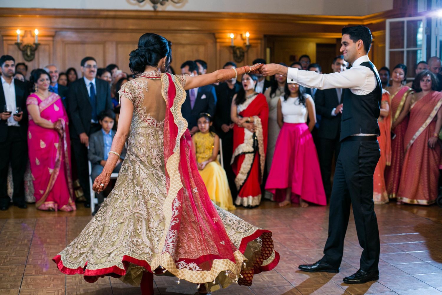Couple performs their first dance in elegant wedding attire surrounded by guests at reception.