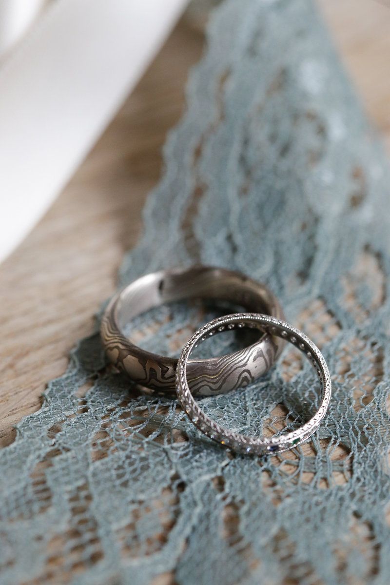 Two silver wedding rings with unique patterns photographed on weathered blue wood.