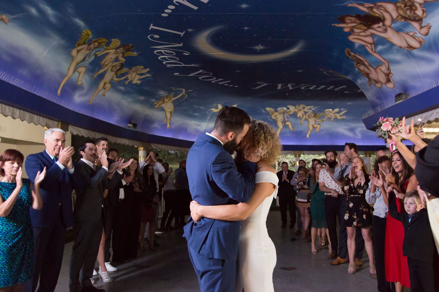 Guests dancing and celebrating at a wedding reception under blue ambient lighting.