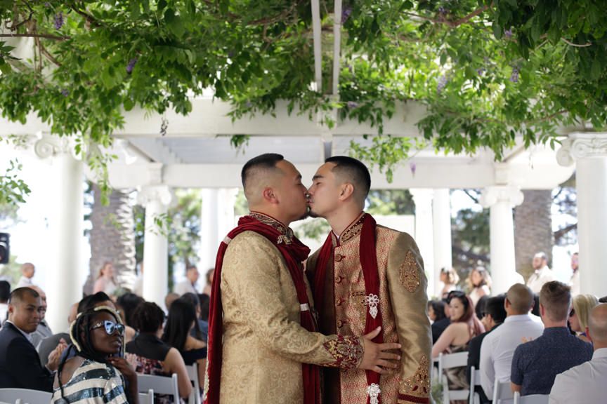 Outdoor wedding celebration with guests mingling under trees and white canopies.