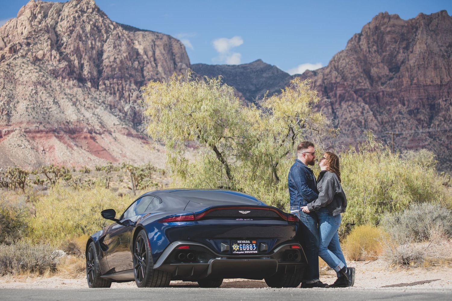 A couple standing by a sports car with red rock mountains in the background.