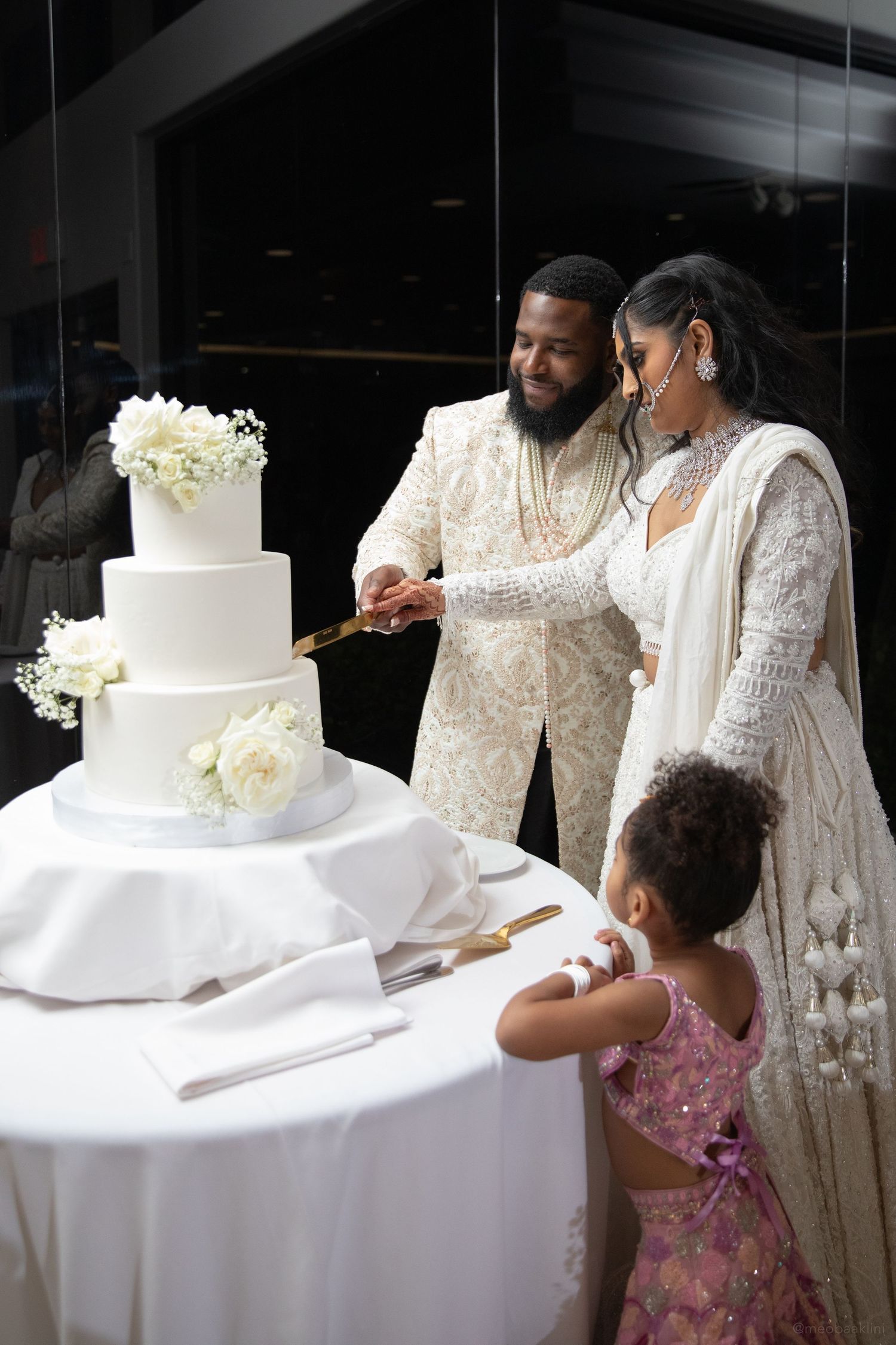 Wedding cake cutting celebration with a small child in a pink dress watching the ceremony.