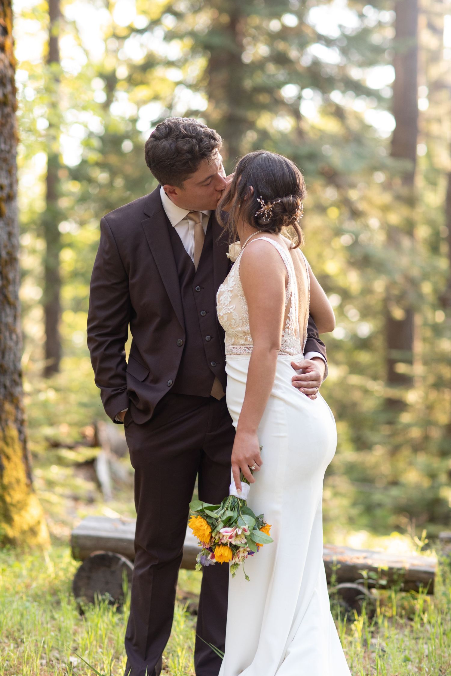 Wedding couple sharing intimate moments in a sunlit forest setting.