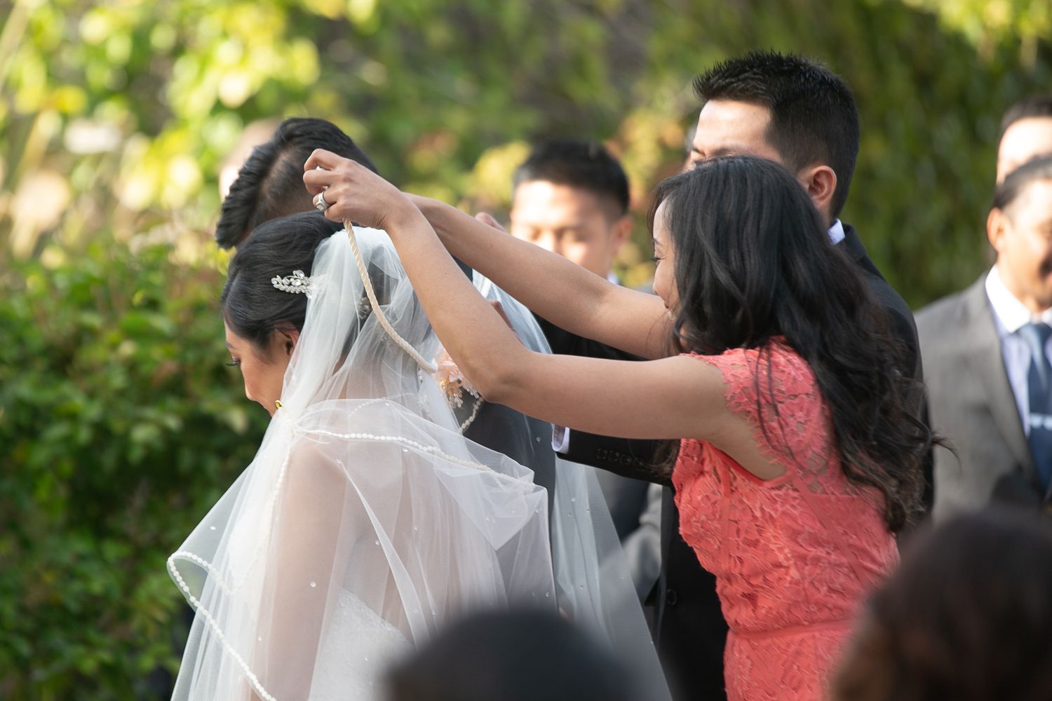 Emotional moment during wedding ceremony with guest adjusting bridal veil.