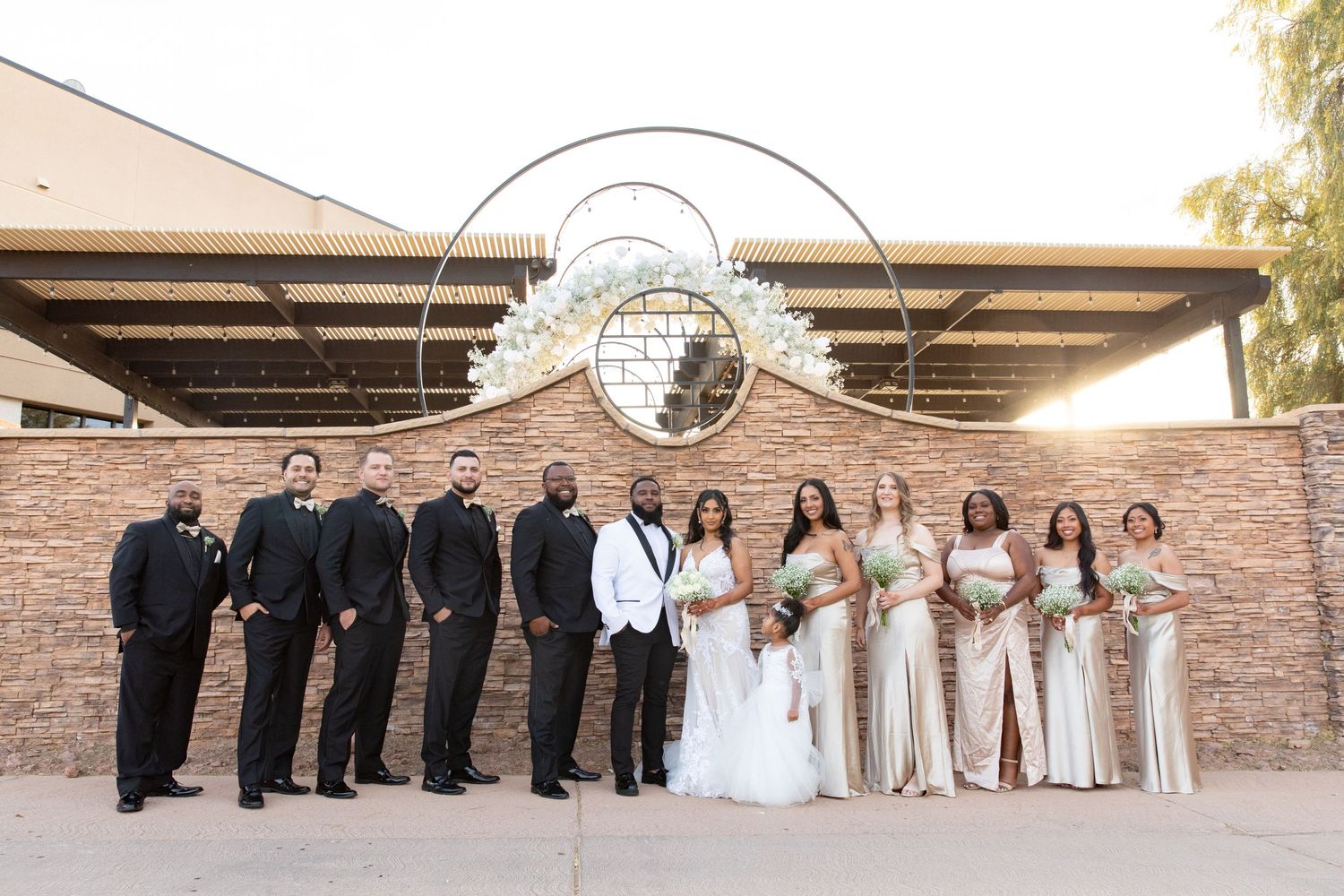 Wedding party poses formally in front of a stone wall with an ornate circular arch.