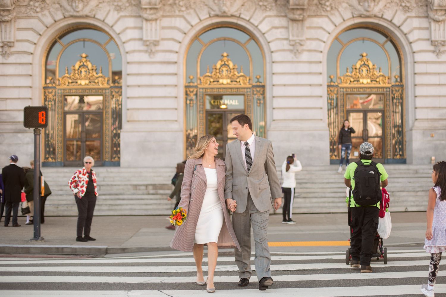 People walking through an elegant marble corridor with classical architectural details and arches.
