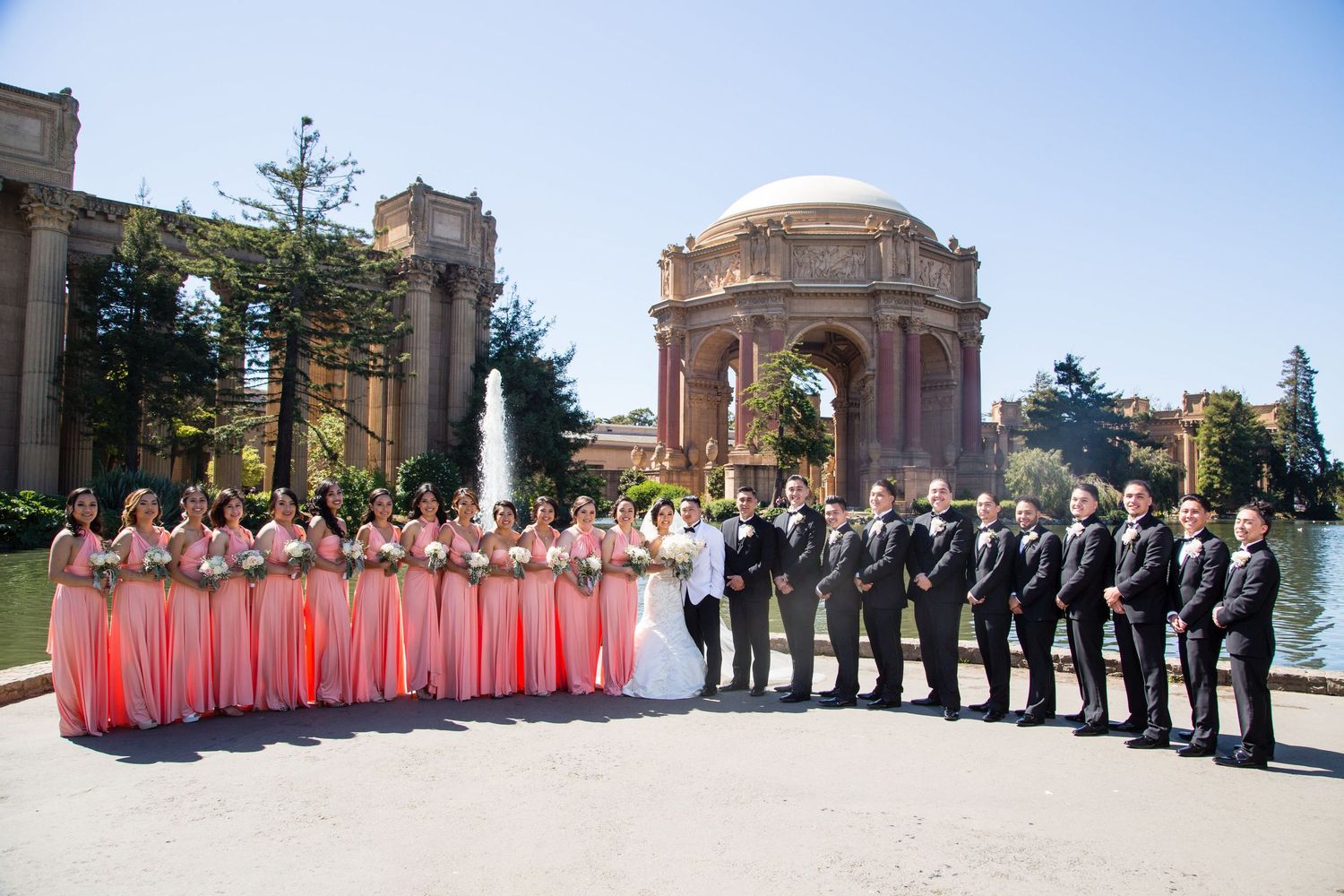Large wedding party in pink and black attire lined up at Palace of Fine Arts.
