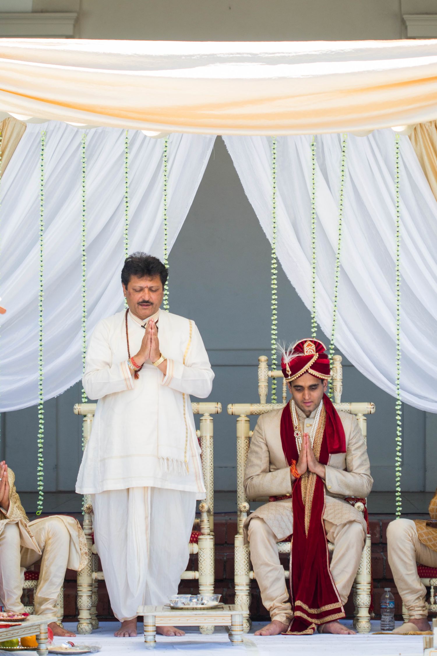 Traditional Hindu wedding ceremony under white mandap with hanging decorations.