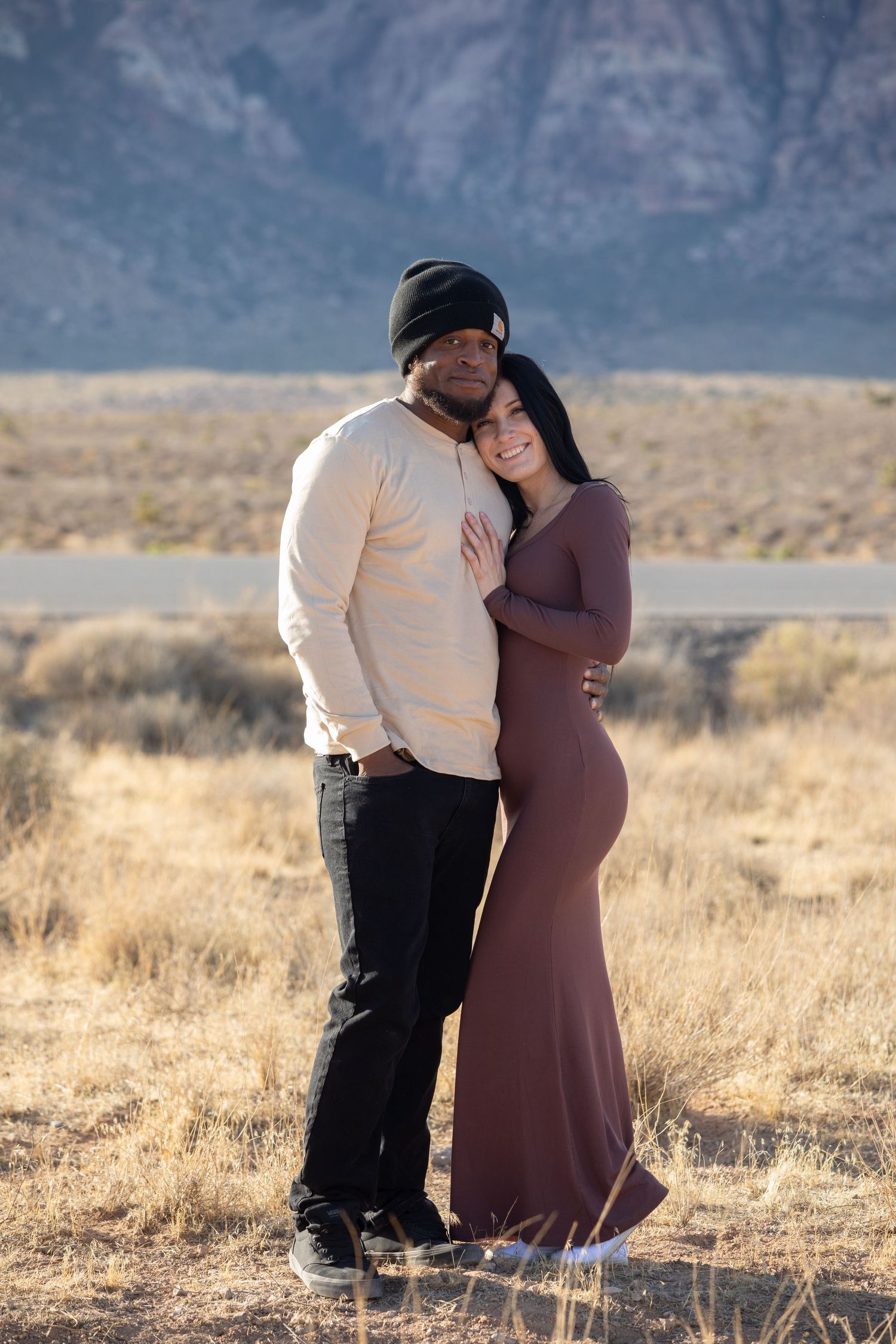 Couple sharing a romantic moment in a desert landscape with mountains in the background at sunset.