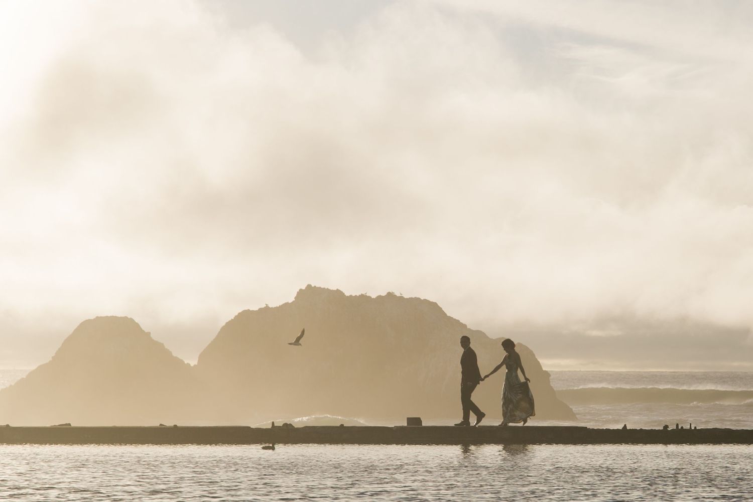 Silhouettes of couples against a mountainous beach landscape at sunset.