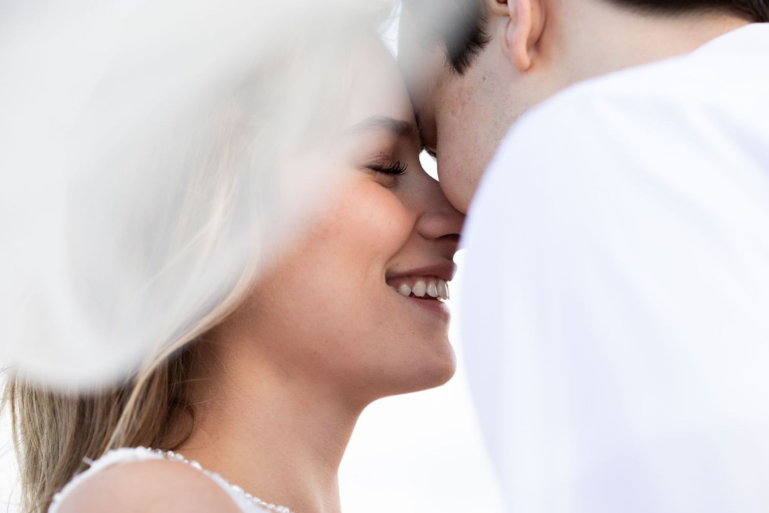 Close up portrait of a couple sharing a tender moment under a white veil.