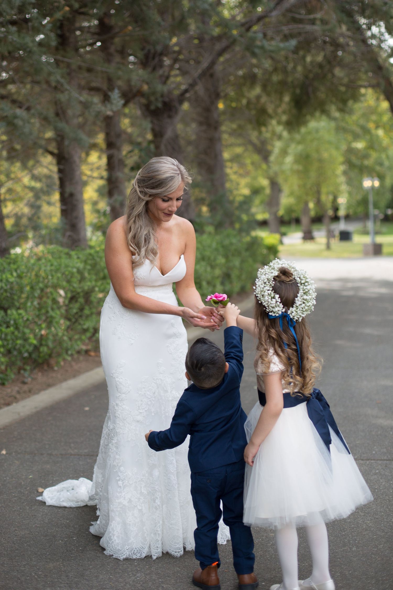 Sweet moment captured on tree-lined path in formal wedding attire.
