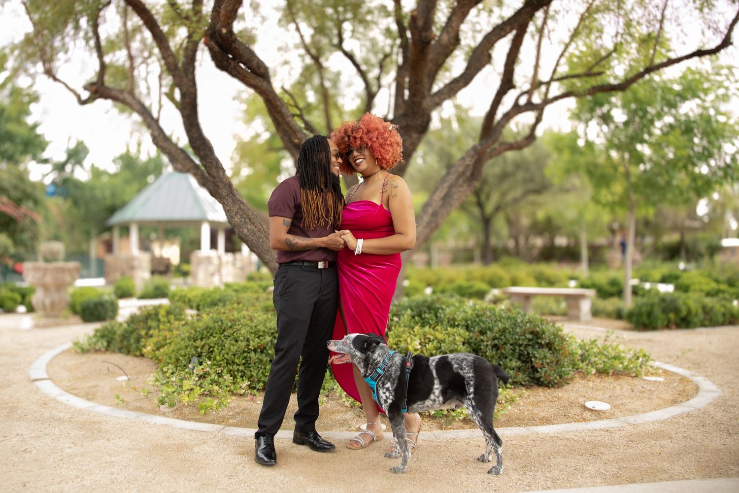 Couple in red and black outfits standing with their dog in a garden path.
