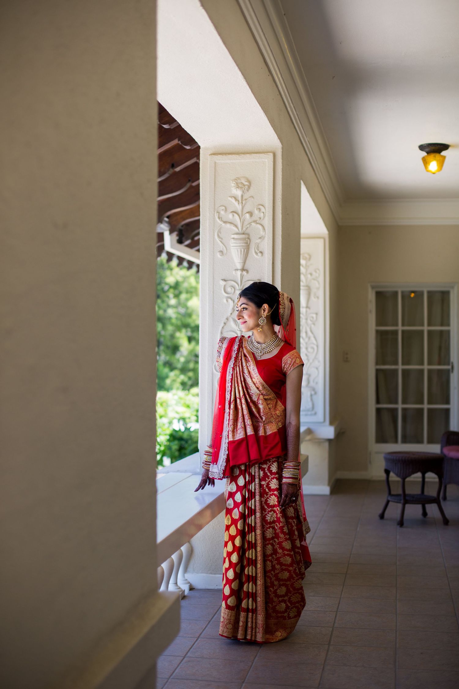 Beautiful traditional Indian bridal outfit in red and gold showcased in an elegant indoor setting with white columns.